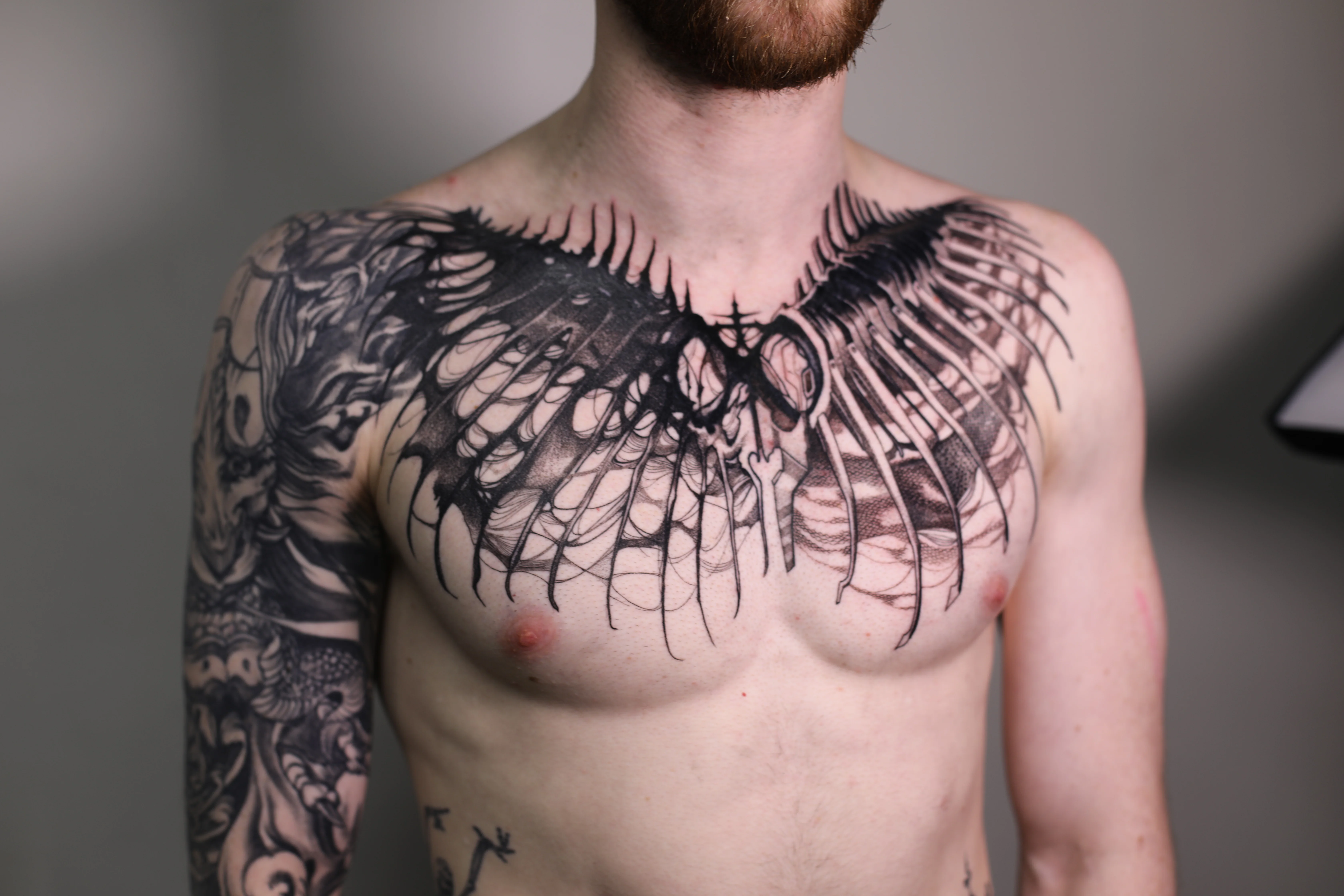 Skeletal Wings Chest Piece with Full Sleeve: skeletal wings, rib cage, cross, arm sleeve with skull and abstract elements, dark, gothic