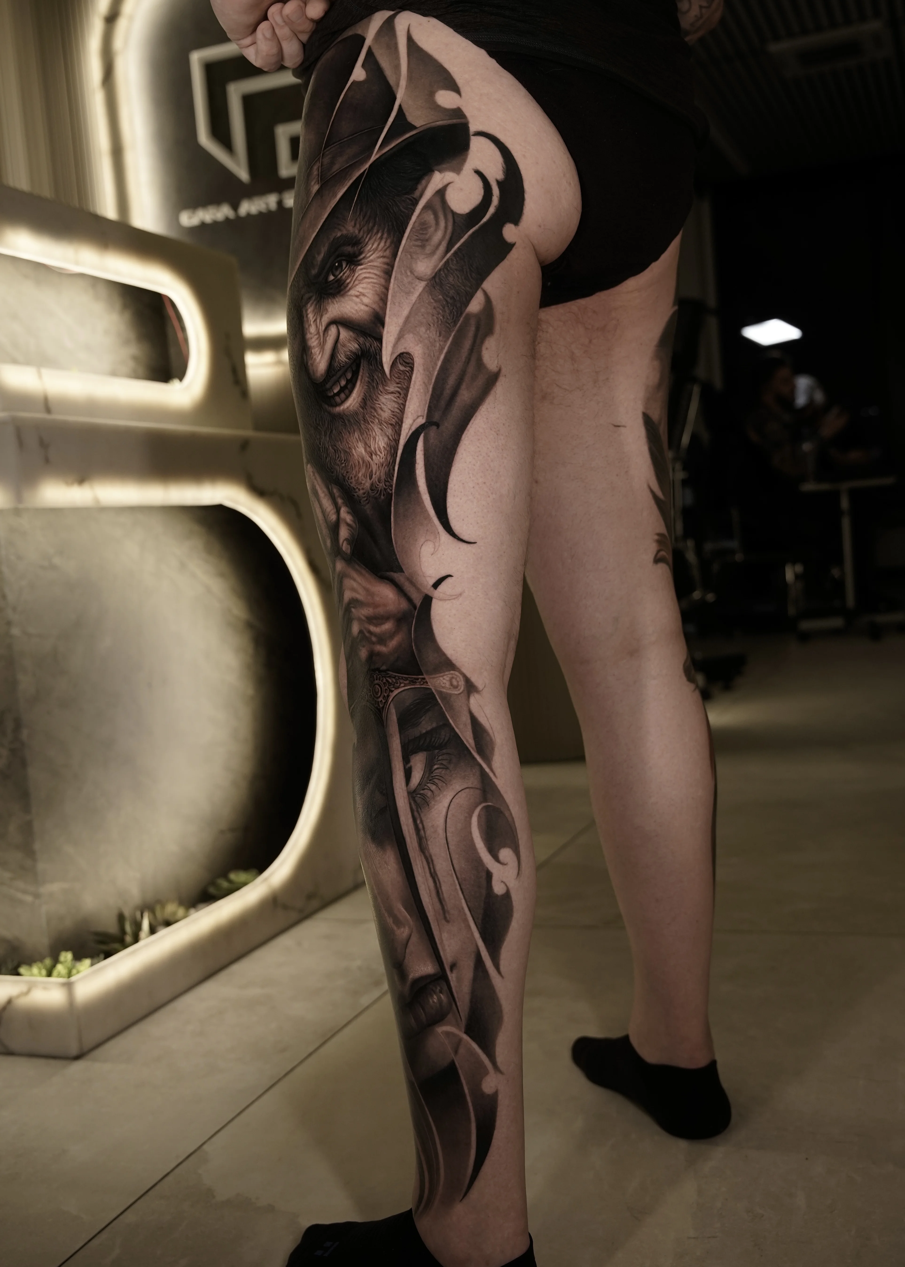 Black & Gray Realism tattoo by Gara: smiling man face, portrait, curved ornamental shapes, dark