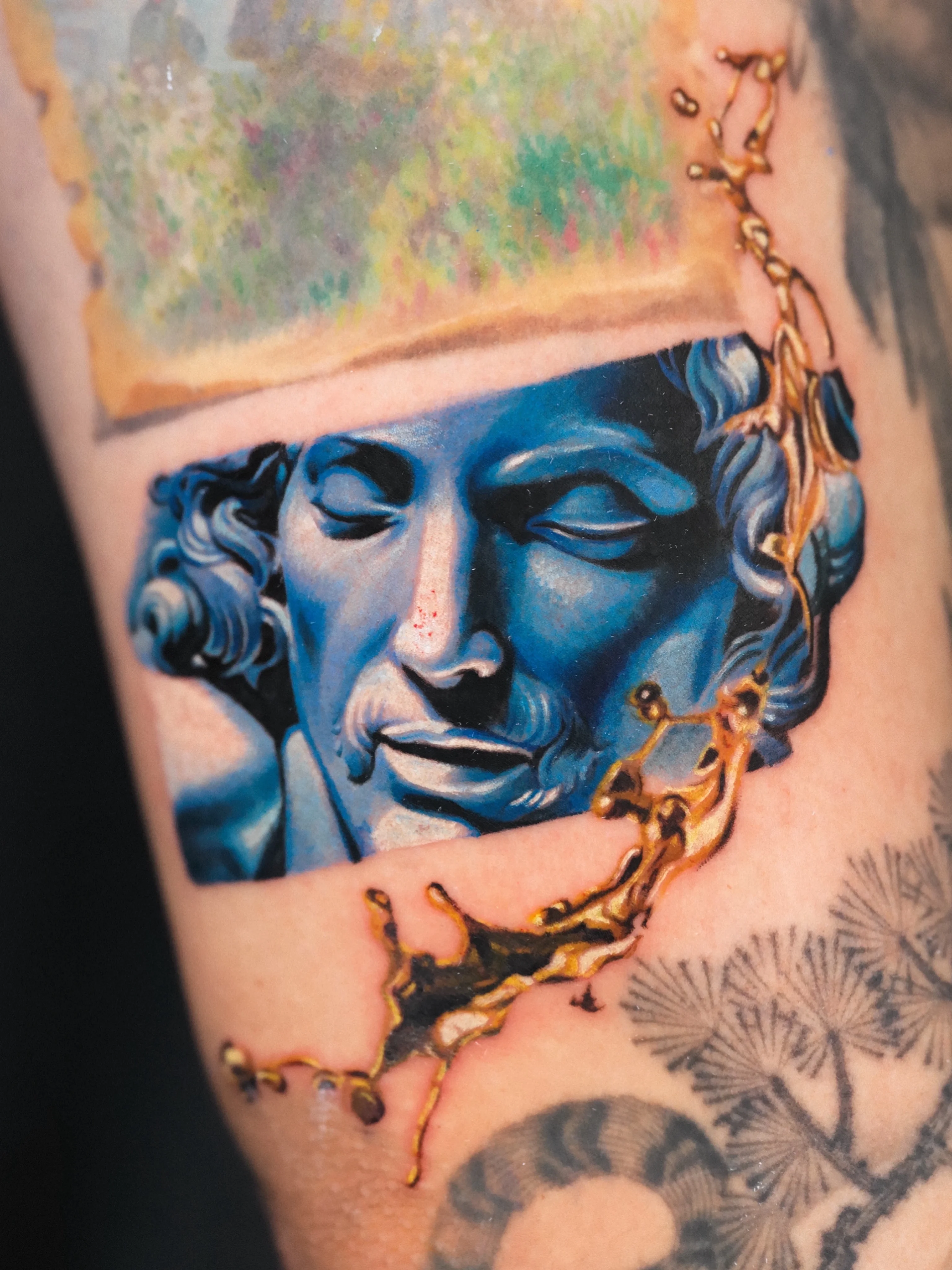 Color Realism tattoo by Q tattoo: male bust sculpture, blue statue face, gold liquid splash, classical sculpture