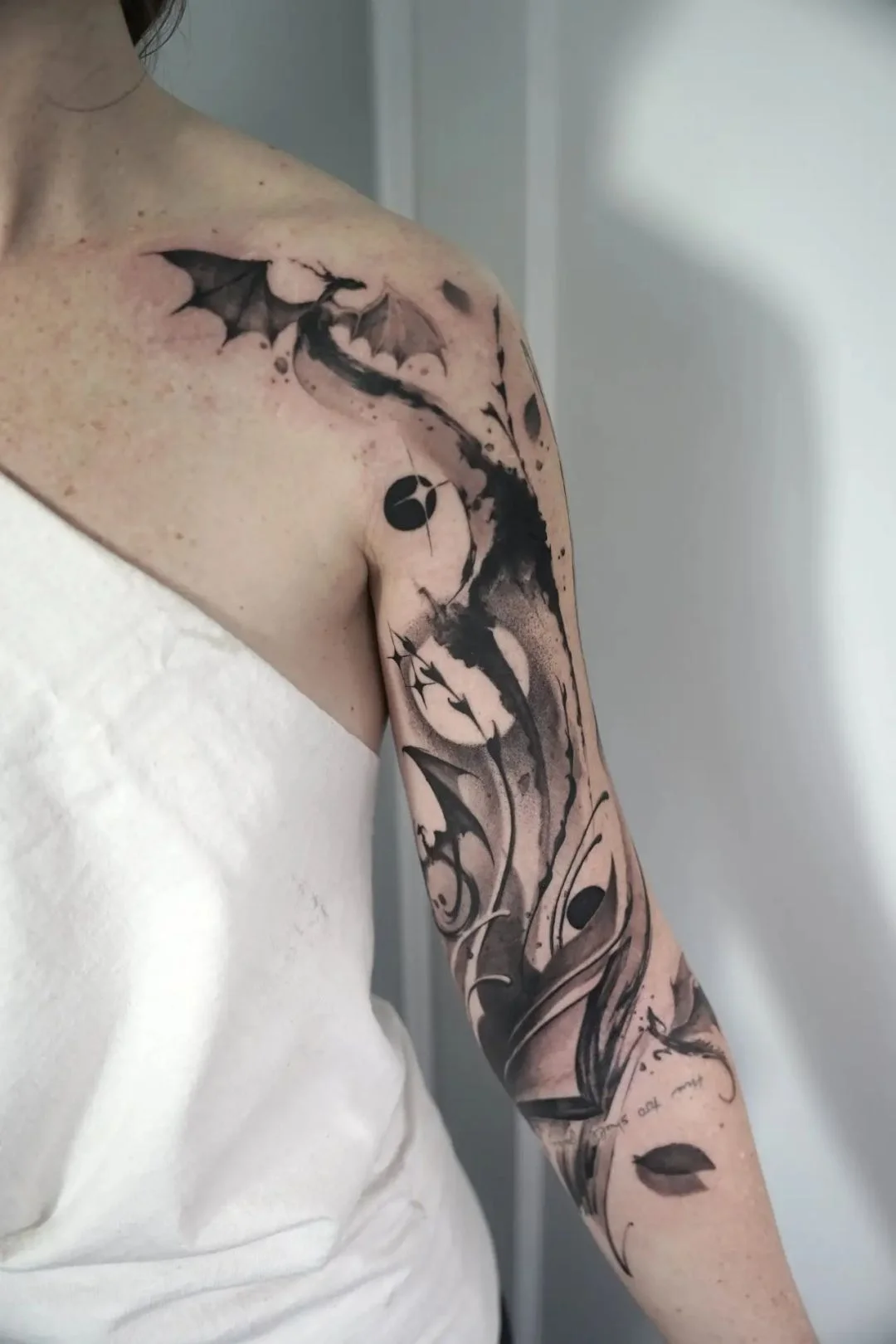 This dynamic, abstract blackwork design depicts a swirling dragon with bold ink splashes and watercolor elements covering the shoulder and a
